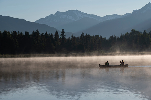 Family paddles canoe on tranquil lake at sunrise on a misty morning