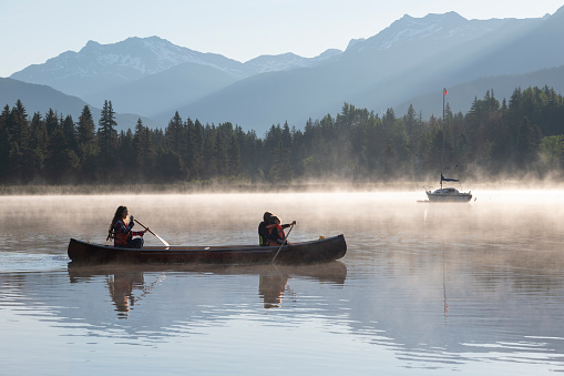 Family paddles canoe on tranquil lake at sunrise on a misty morning