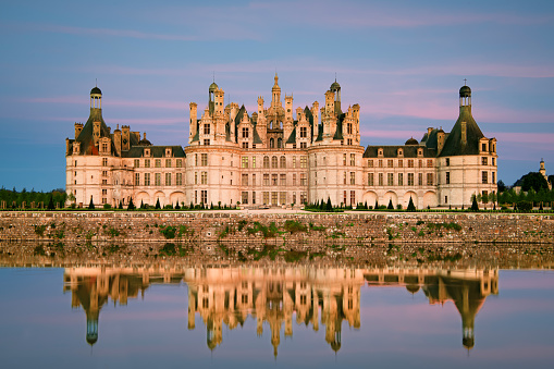Chambord, France - May 22, 2017: View of Chambord Castle reflected in the decorative moat at sunset. Copy space in sky.