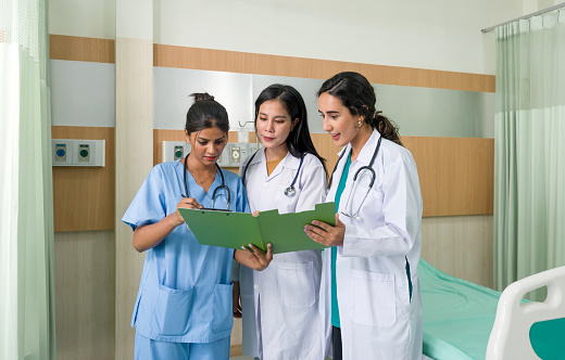 Three female doctors are in a hospital room. They're studying a medical file intently.