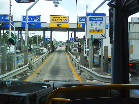 Civitavecchia, Italy- 09/19/2011:\nBus is entering the toll road gate in Italy.\nRiservata Clienti Telepass means reserved for Telepass customers.\nTelepass is the brand name for an electronic toll collection system used to collect toll (pedaggio) on motorways (autostrade) in Italy operated by Autostrade per l'Italia S.p.A., its affiliates, and other legal entities. The system was introduced in 1989.