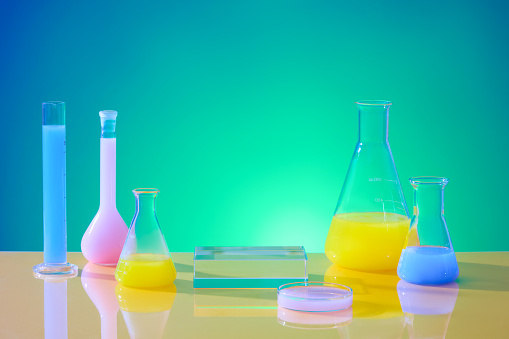 Glassware filled with colored liquids is showcased against a blue-green gradient backdrop. Utilizing laboratory space for front-view advertising purposes. Empty podium for display.