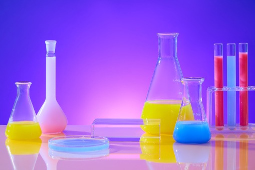 Frontal perspective of vibrant liquids in glassware on a pink-purple gradient backdrop. Vacant area for product exhibition in a simulated experiment setting.