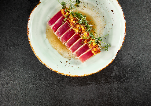 Sliced tuna tataki with mango salsa and ponzu sauce, elegantly served on a ceramic plate.