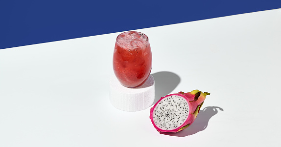 An exotic lemonade with dragon fruit, elegantly perched on a white pedestal, complemented by a bold blue background.