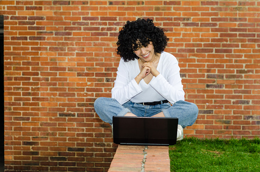 portrait of young beautiful white woman with curly hair working with laptop outdoors