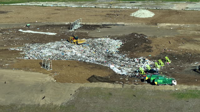 Garbage landfill site with bulldozer tractors burying large amount of trash under the ground. Harmful impact of open waste management on environment