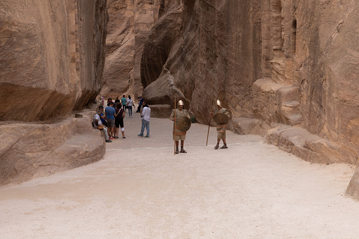 Wadi Musa, Jordan, October 05, 2023 : Two Bedouins dressed in uniform of Nabatean warriors stand for tourists in front of the entrance to the gorge Al Siq in Petra in Wadi Musa city in Jordan
