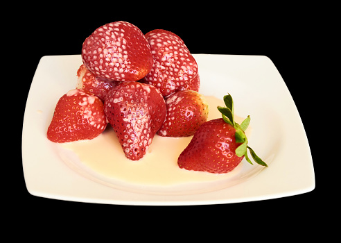 Ripe strawberries covered with yogurt on a square white plate on a black background isolated