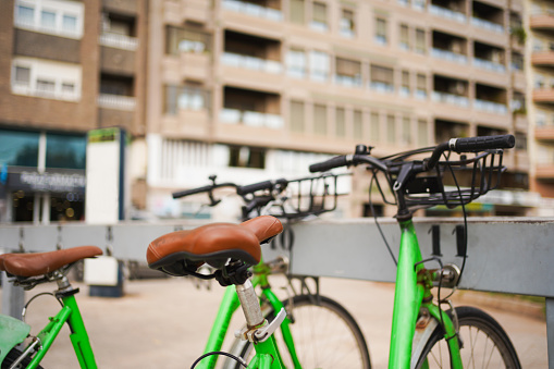 Green bicycles in bike rack with urban building background.