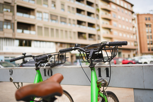 Green bicycle parked in an urban bike rack with buildings in the background.
