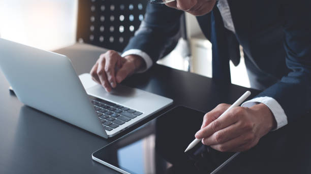 istock Businessman using stylus pen signing e-document or business contract on digital tablet via mobile app with laptop computer on office desk. E-signing, electronic signature, business concept 1923985948