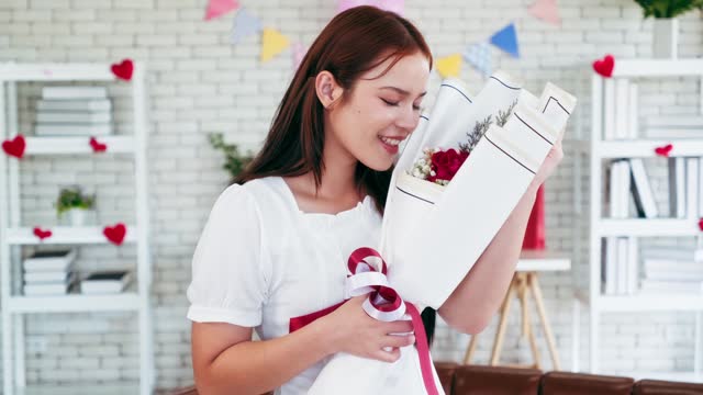 Attractive Asian young adult woman in love, holding a floral bouquet gift from her boyfriend and smelling the flowers in a happy mood. International Women's Day. Valentine's Day celebration concept.