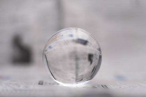 A glass globe reveals the letters inside, with a newspaper in the background.