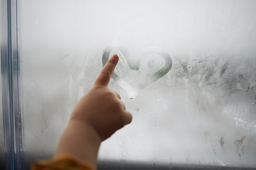 Beautiful girl drawing with finger on blurred window. Winter time.