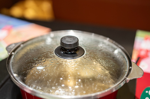 A hotpot kettle with boiling water is placed on the electric stove on the dining table. Close-up at the glass lid. Food utensil object photo. close-up and selective focus.