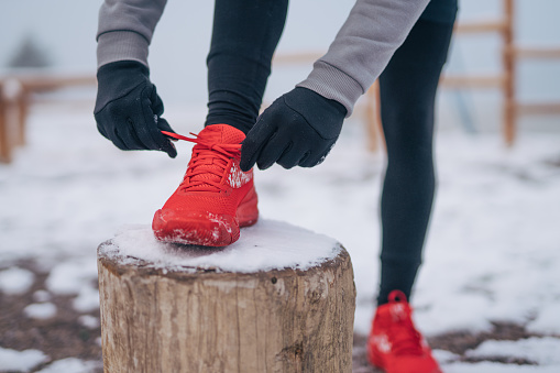Young man tying running shoes and making pause during stretching and exercises in the winter training outside