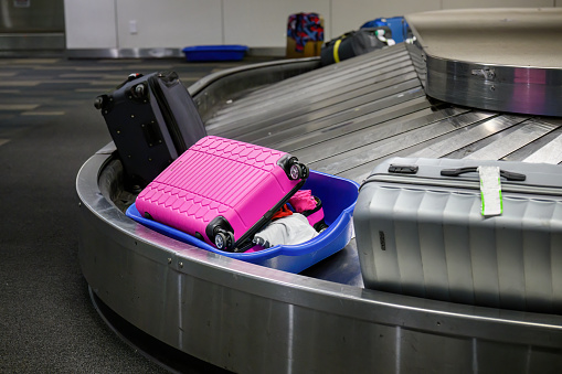 Broken suitcase placed in a plastic basket. Suitcases on luggage conveyor belt in baggage claim at airport.