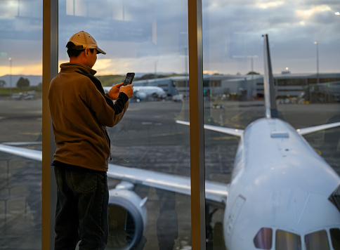 Man taking photos using smartphone of an aeroplane at the airport terminal.