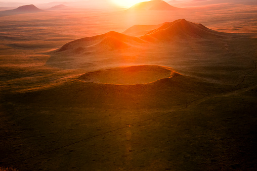 Vulkankrater in der Steppe der Mongolei im orangenen Gegenlicht der unter- oder  aufgehenden Sonne am Horizont