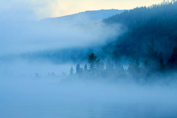 View over forest with morning fog. Dawn over the foggy lake Yazevoe. Beautiful dreamy view.  \nLake Yazevoe is located at an altitude of 1685 meters above sea level. It is part of the State National Natural Park \
