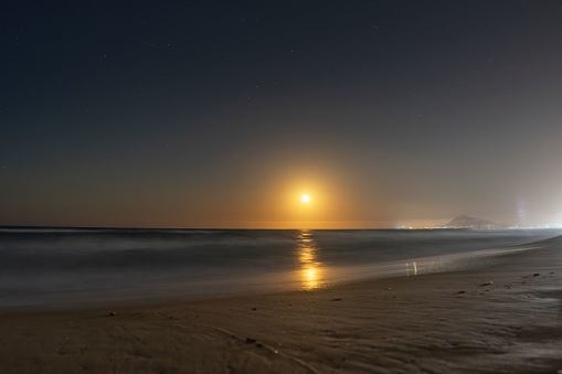 Close-up of Gandia beach with moonrise in the background of the photo. Night beach with fine brown sand. Seascape. Inspiring and relaxing sunset.
