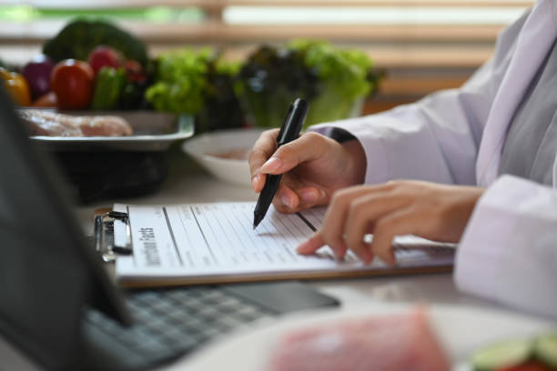 istock Side view of nutritionist writing diet plan and using laptop at desk with different healthy products 1924251402