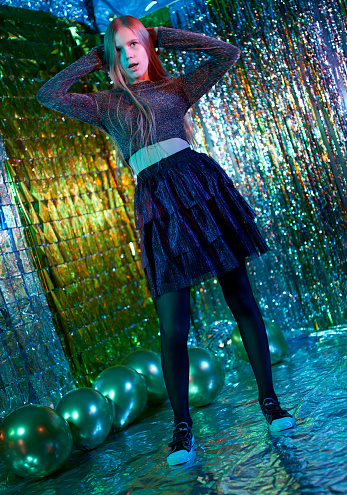 Beautiful fair-haired girl dressed in cocktail dress is dancing a modern dance. Studio shooting on a disco party on a glittering background
