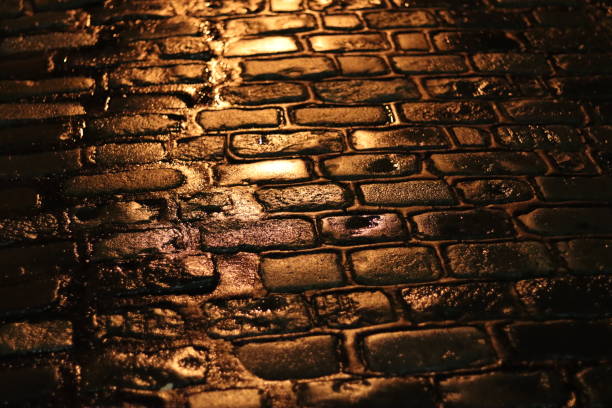 istock Wet cobblestones on a street at night, illuminated by a light 1924263812