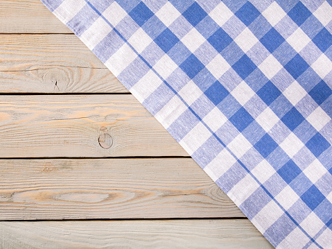 Rustic wooden background with a blue checkered napkin, creating a cozy and inviting setting for text space. Perfect for food and kitchen-related designs.