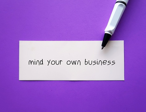 On purple background, pen writing on paper MIND YOUR OWN BUSINESS, to tell someone rude way to stop asking private questions which is none of their business