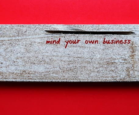 Rough texture wood on red background with text written MIND YOUR OWN BUSINESS, to tell someone rude way to stop asking private questions which is none of their business