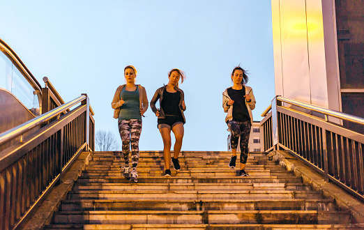 Group of young women friends team training running down stairs in town on sunset