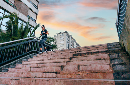 Happy young female runner training down stairs in urban runway with palm trees on sunset