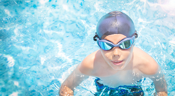 Active, happy child (boy) in cap, sport goggles ready to learns professional swimming in swimming pool. Kid enjoying water. Healthy lifestyle. Copy space. Empty plase.