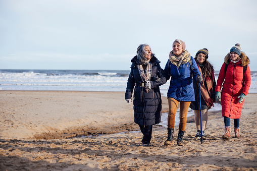 Wide shot of a group of mature female friends on a walk in Tynemouth, North East England. They are enjoying time outside on a beach.