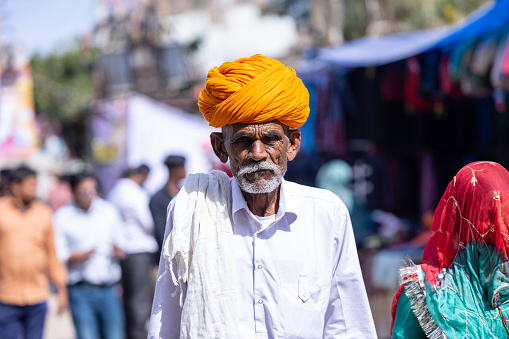 Pushkar, Rajasthan, India - November 2022: Pushkar fair, Portrait of an rajasthani old male with in white traditional dress and colorful turban at pushkar fair ground.