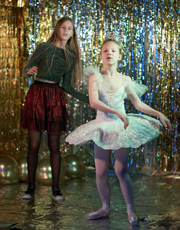 Preteen girls dressed in different clothes (cocktail dress and ballet tutu). They are dancing together. Studio shooting on a New Year's disco party