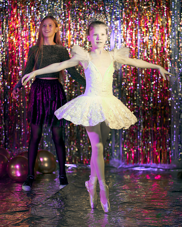 Preteen girls dressed in different clothes (cocktail dress and ballet tutu). They are dancing together. Studio shooting on a New Year's disco party