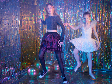 Preteen girls dressed in different clothes (cocktail dress and ballet tutu). They are dancing together. Studio shooting on a New Year's disco party