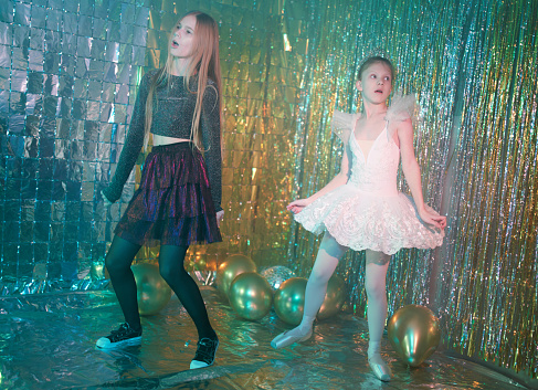 Preteen girls dressed in different clothes (cocktail dress and ballet tutu). They are dancing together. Studio shooting on a New Year's disco party