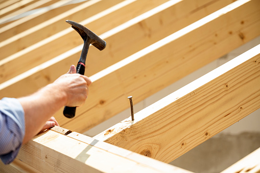 A roofer hammering a nail into a wooden beam of a new house for the topping-out ceremony.