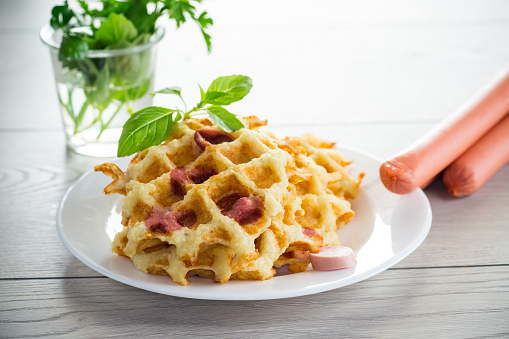 cooked fried potato waffles with sausage stuffing inside, in a plate on a wooden table.