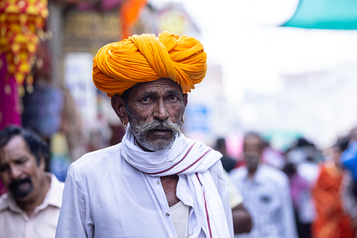 Pushkar, Rajasthan, India - November 2022: Pushkar fair, Portrait of an rajasthani old male with in white traditional dress and colorful turban at pushkar fair ground.