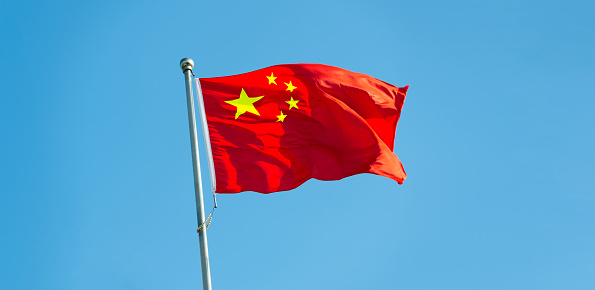 Chinese flag on pole waving in the wind against blue sky