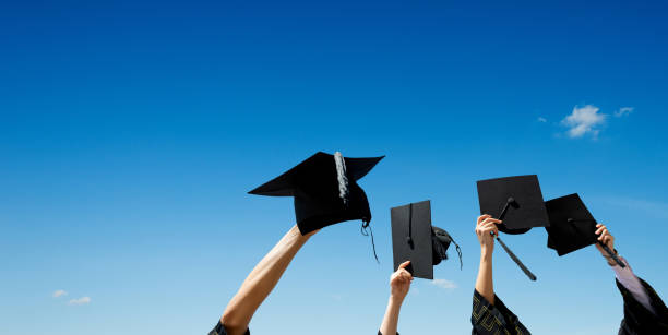 Four hands holding graduation hats against blue sky