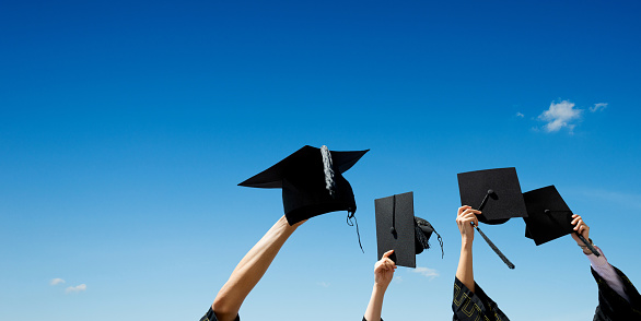 Four hands holding graduation hats against blue sky