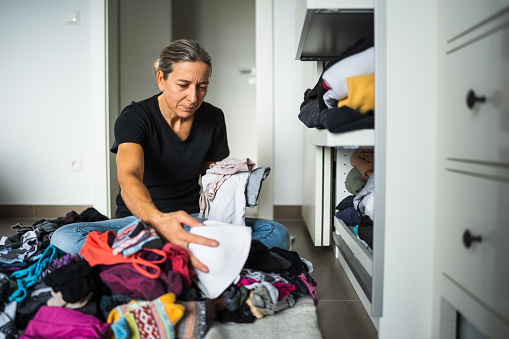 one mature adult woman sitting on floor in dressing room of her house sorting out and reducing her clothes