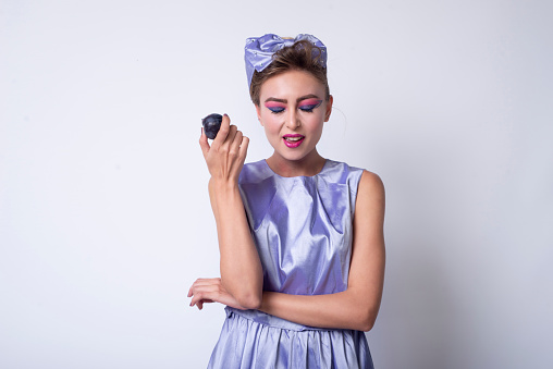 Girl in purple dress holding a plum and she grimaces. Fashion Photography.