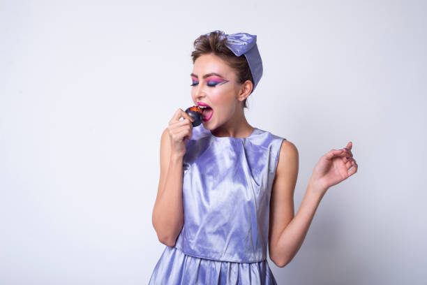 girl in purple dress eating a plum and she grimaces. - plum eating women fruit стоковые фото и изображения